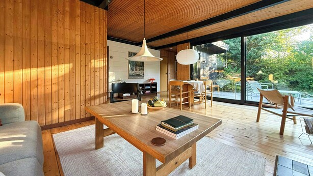 A modern interior with wooden walls, a dining area, and a view of greenery outside. - 60s modernism by Rågeleje beach (Vejby)