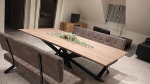 A dining area with a long wooden table, cushioned benches, a television on a wooden cabinet, and a window with a sheer curtain. - On the wine route and Christmas markets (Beblenheim)