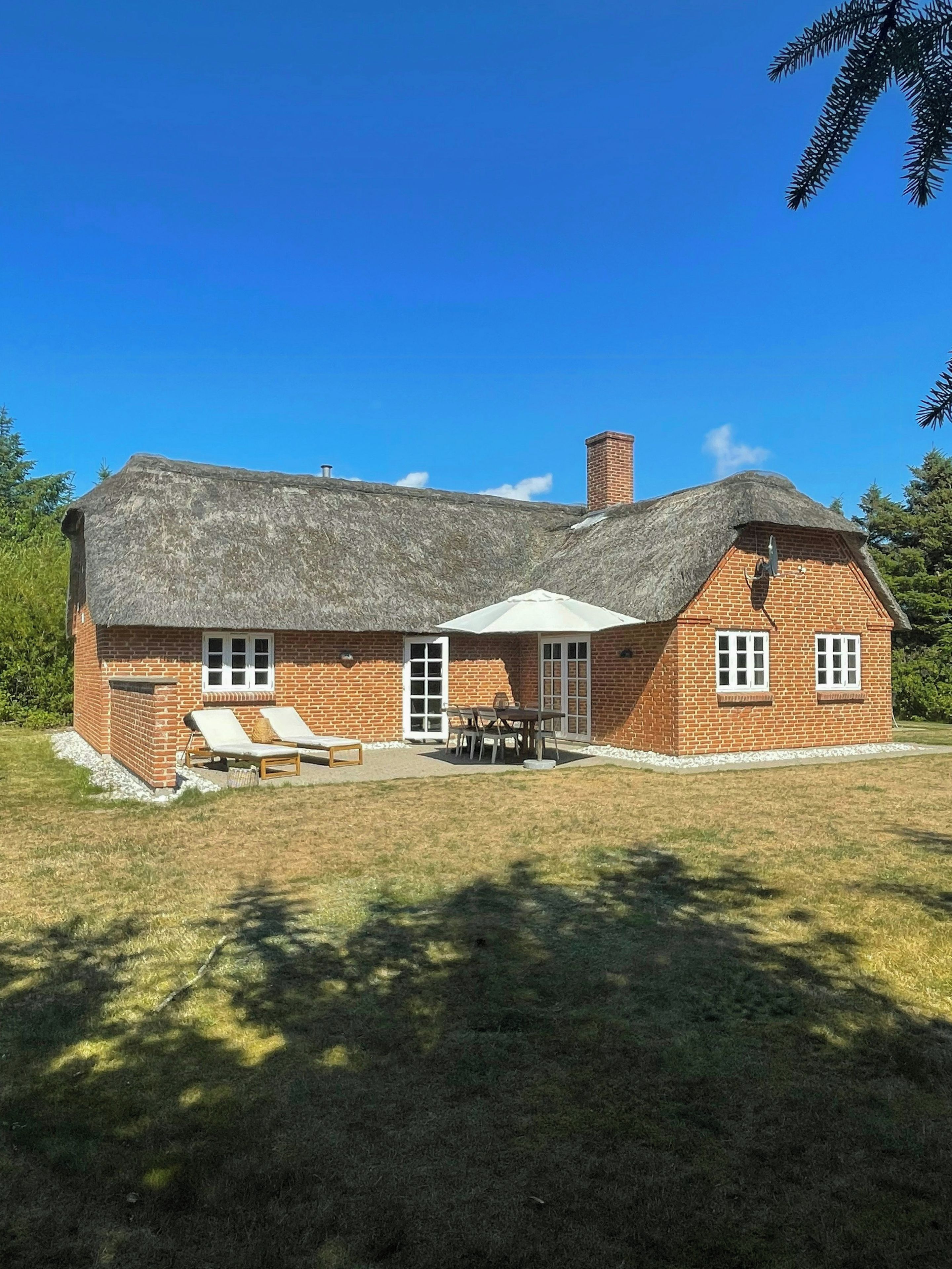 A two-story brick house with a thatched roof, a patio with outdoor furniture, and a well-maintained lawn.