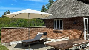 Une terrasse avec une table et des chaises, un barbecue et un bâtiment à toit de chaume.