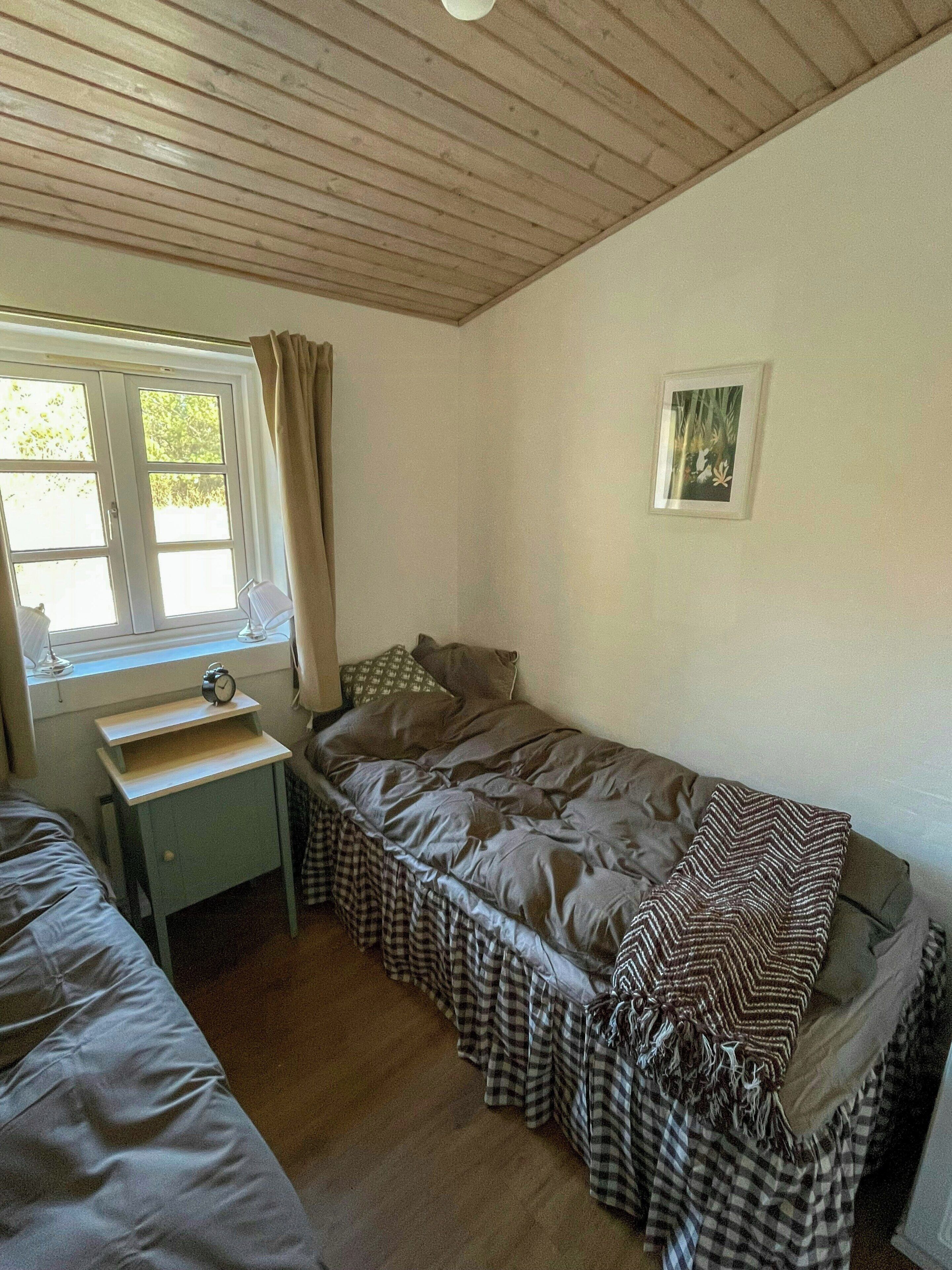 Un dormitori amb un llit individual, una taula de nit, una finestra amb cortines i un quadre encimbellat a la paret.