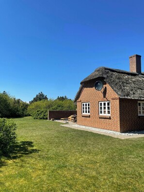 A brick house with a thatched roof, a chimney, and a small garden with a bench and table. - Charming west coast house near Vedersø Klit Strand (Ulfborg)