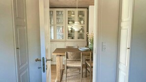 Une pièce avec un plancher en bois, une table à manger avec des chaises, un buffet avec des portes en verre et une porte donnant sur une autre pièce.