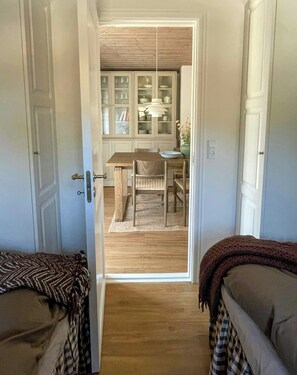 Ein Zimmer mit Holzboden, einem Esstisch mit Stühlen, einer Vitrine mit Glastüren und einer Tür zu einem anderen Raum.