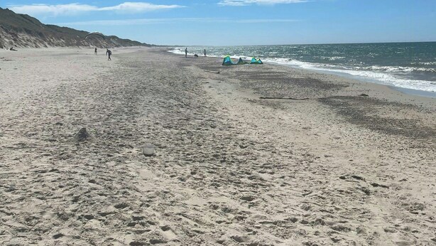 Une vaste plage de sable, parsemée d’empreintes, avec quelques tentes et un ciel bleu dégagé.