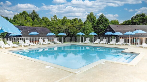 A swimming pool with lounge chairs and umbrellas, surrounded by trees and a clear sky. - Cosy Apartment Near Egletons Town (Egletons)