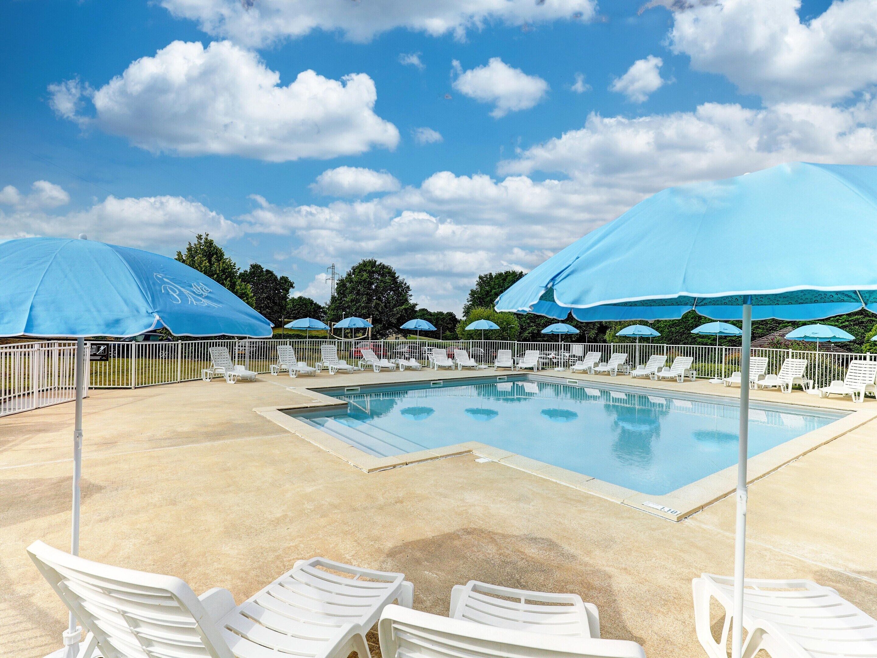 A swimming pool with white lounge chairs and blue umbrellas, surrounded by a white fence.