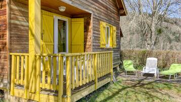 A wooden cabin with yellow shutters, a porch, and two green chairs outside.