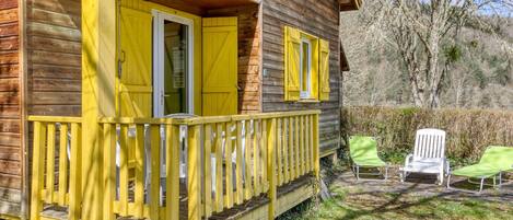 A wooden cabin with yellow shutters, a porch, and two green chairs outside.
