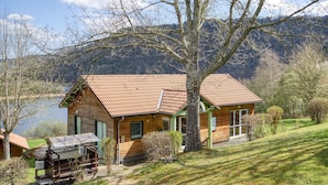 Een houten chalet met pannendak, gelegen aan een meer met bergen op de achtergrond.