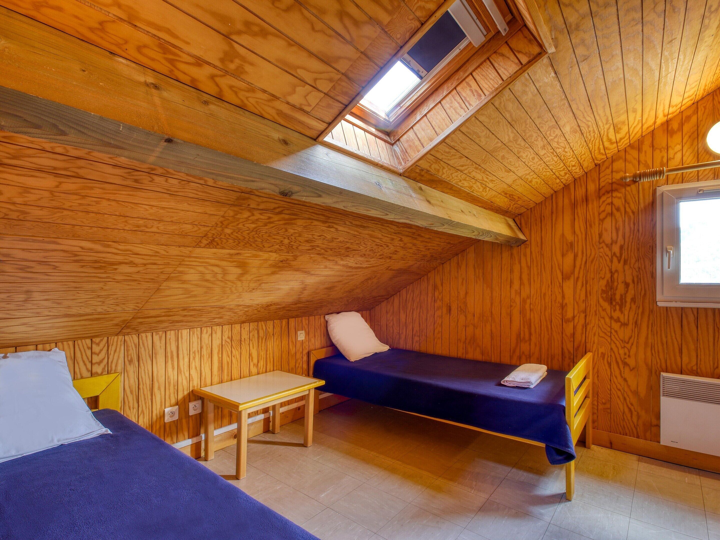 Une petite pièce aux murs lambrés, avec un lit en mezzanine, un bureau et une fenêtre.