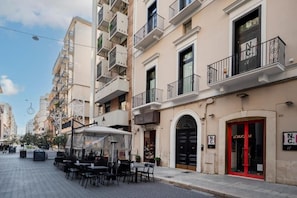 Une rue bordée de terrasses, un café et un immeuble avec une porte rouge et des balcons.