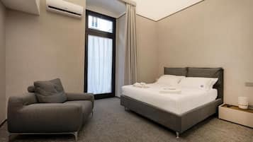 Una habitación de hotel moderna con una cama, un sofá, un aire acondicionado, una ventana con cortinas y una mesita de noche con lámpara.