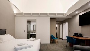 Une chambre d’hôtel équipée d’un lit, d’un bureau, d’une chaise, d’une télévision et d’une salle de bain visible à travers une porte.