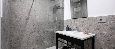 Une salle de bain moderne avec une douche à parois de verre, un lavabo blanc doté d’un plan de travail noir et un miroir au-dessus du lavabo.