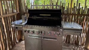 An outdoor grill area with a stainless steel grill, a wooden deck, and a bamboo fence.
