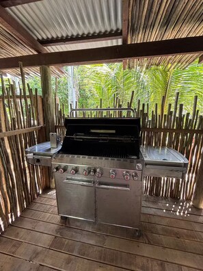 An outdoor grill area with a stainless steel grill, a wooden deck, and a bamboo fence.