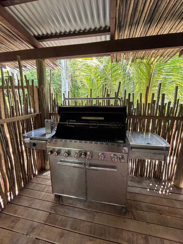 Un espace barbecue extérieur comprenant un gril en acier inoxydable, une terrasse en bois et une clôture en bambou.