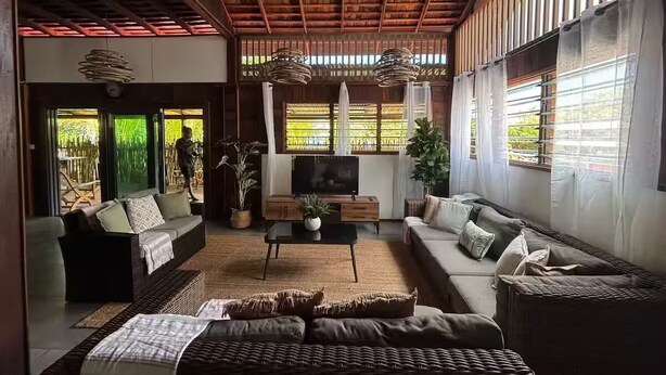 A spacious living room with a high ceiling, large windows, a flat-screen TV, and comfortable seating.
