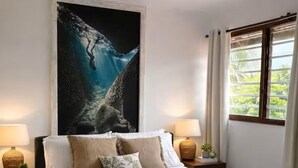 A bedroom with a bed, two bedside lamps, a nightstand, a large painting, and a window with curtains.