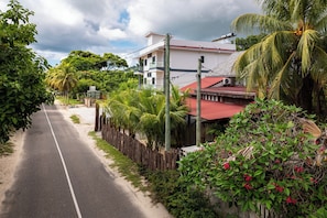 A quiet street lined with lush greenery and a two-story building with a red roof.