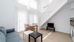 Ett modernt vardagsrum med en soffa, ett matbord, stolar, en tv och en trappa.