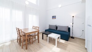 Ett rum med ett matbord i trä, stolar, en blå soffa, ett litet vitt bord, en golvlampa och en tavla på väggen.