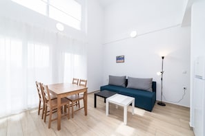 A room with a wooden dining table, chairs, a blue sofa, a small white table, a floor lamp, and a painting on the wall. - Sea& Salt- Panoramic Terrace BBQ Starlink WiFi  2-bedroom Loft Paralia Ofriniou (Paralia Ofriniou)