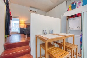 Une pièce avec une table en bois, un lit, un escalier et un lave-linge.
