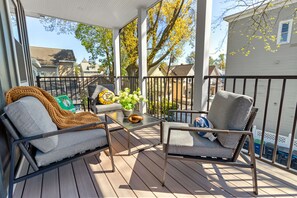 A covered porch with two grey cushioned chairs, a small table with a plant, and a yellow sign. - Bostonian 2BR2BTH / 8 Minutes to Boston (Somerville)