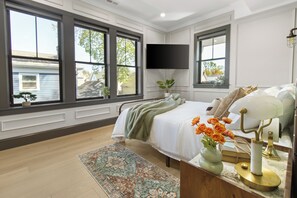 A bedroom with a bed, a flat-screen TV, a window with a view, and a bedside table with a lamp. - Bostonian 2BR2BTH / 8 Minutes to Boston (Somerville)