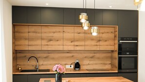Une cuisine moderne avec des meubles en bois, un plan de travail noir, une machine à café et un vase rempli de fleurs.