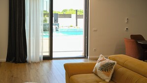 Un salon avec un canapé, une table basse et une vue sur une piscine, visible à travers une porte vitrée.