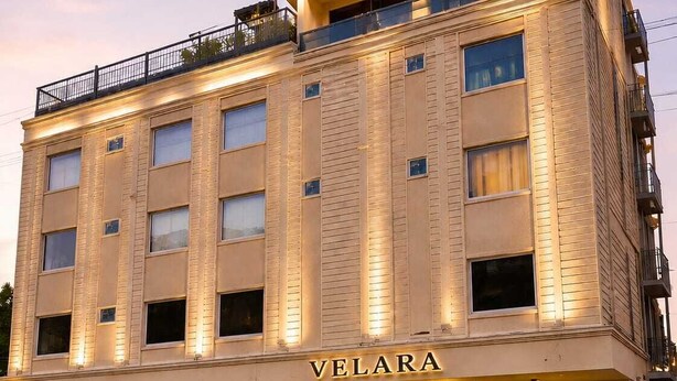 Un hotel de varios pisos con un llamativo letrero 'VELARA', que presenta una fachada moderna con ventanas amplias y techo plano.