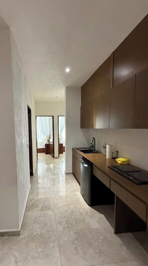Eine moderne Küche mit Geschirrspüler, Spüle und Holzschränken. Ein Flur führt zu einem Schlafzimmer mit Bett und Vorhängen.