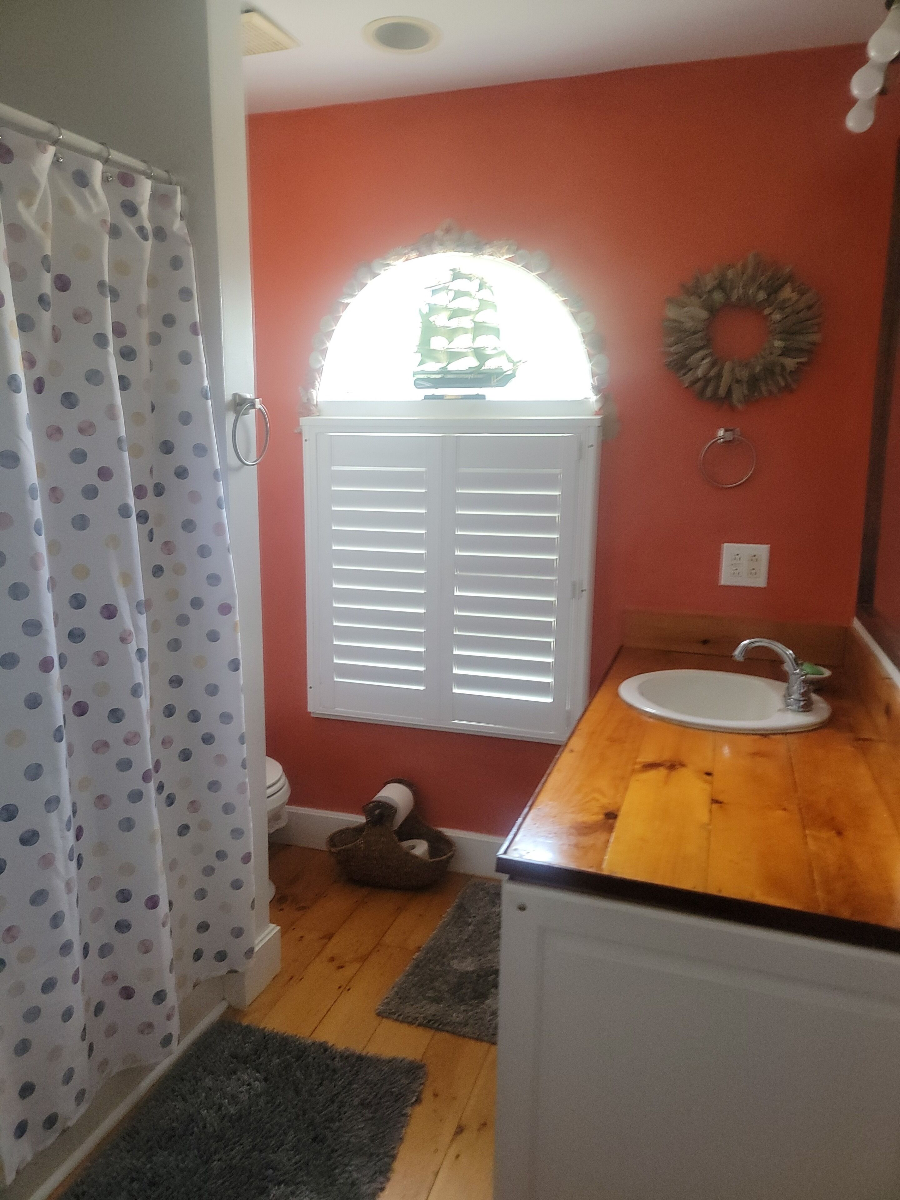 A bathroom with a shower curtain, a window with blinds, a sink, and a wooden countertop.