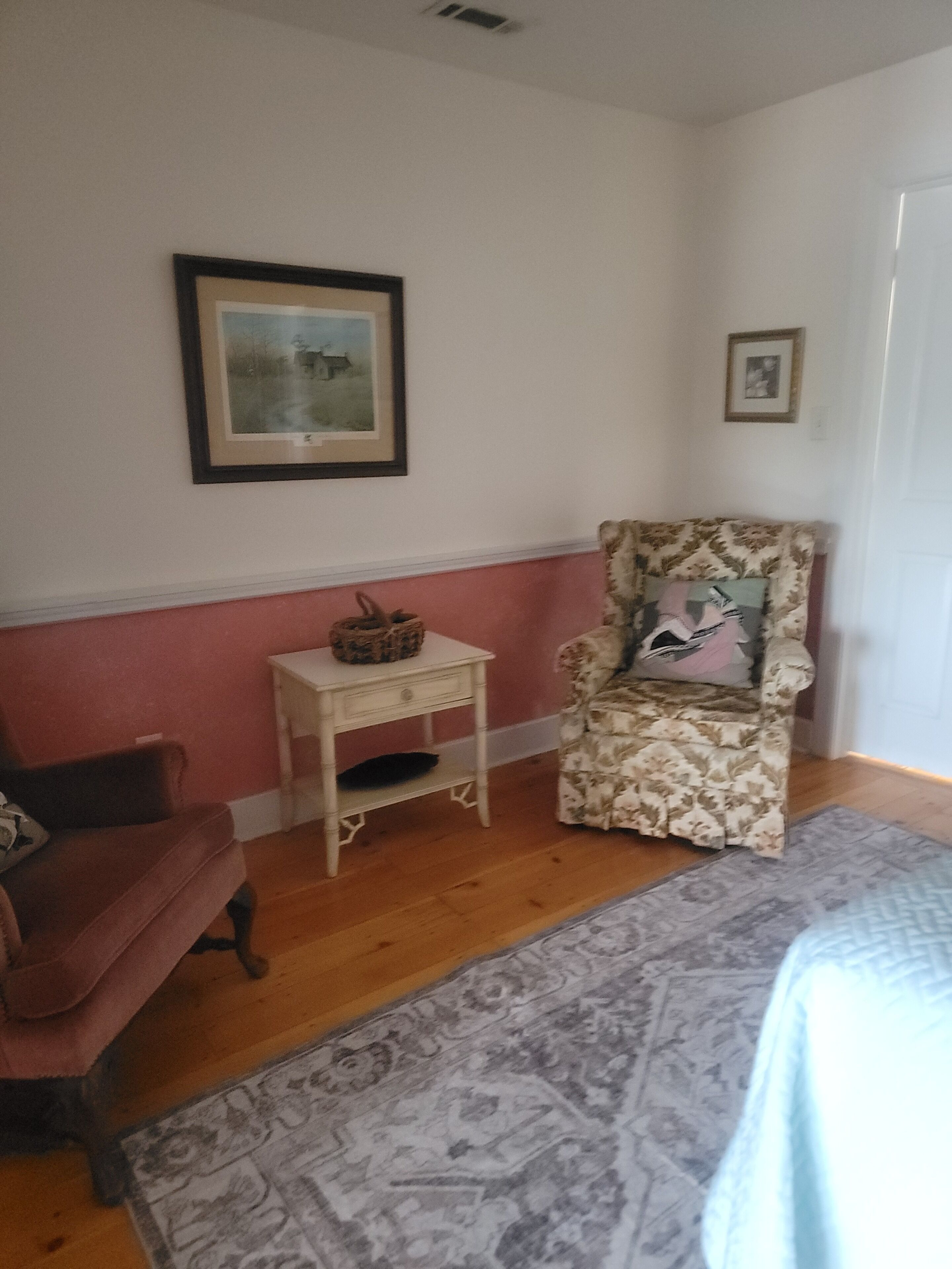 Une pièce comprenant un fauteuil à motifs, une petite table d’appoint, un tableau encadré accroché au mur et un tapis à motifs posé sur le sol.