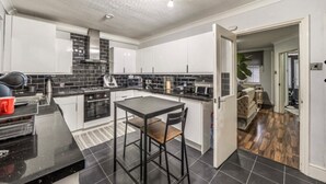 A modern kitchen with black countertops, white cabinets, and a dining area with a table and chairs. - Baoyan Greenwich spacious 3 bedrooms house (London)