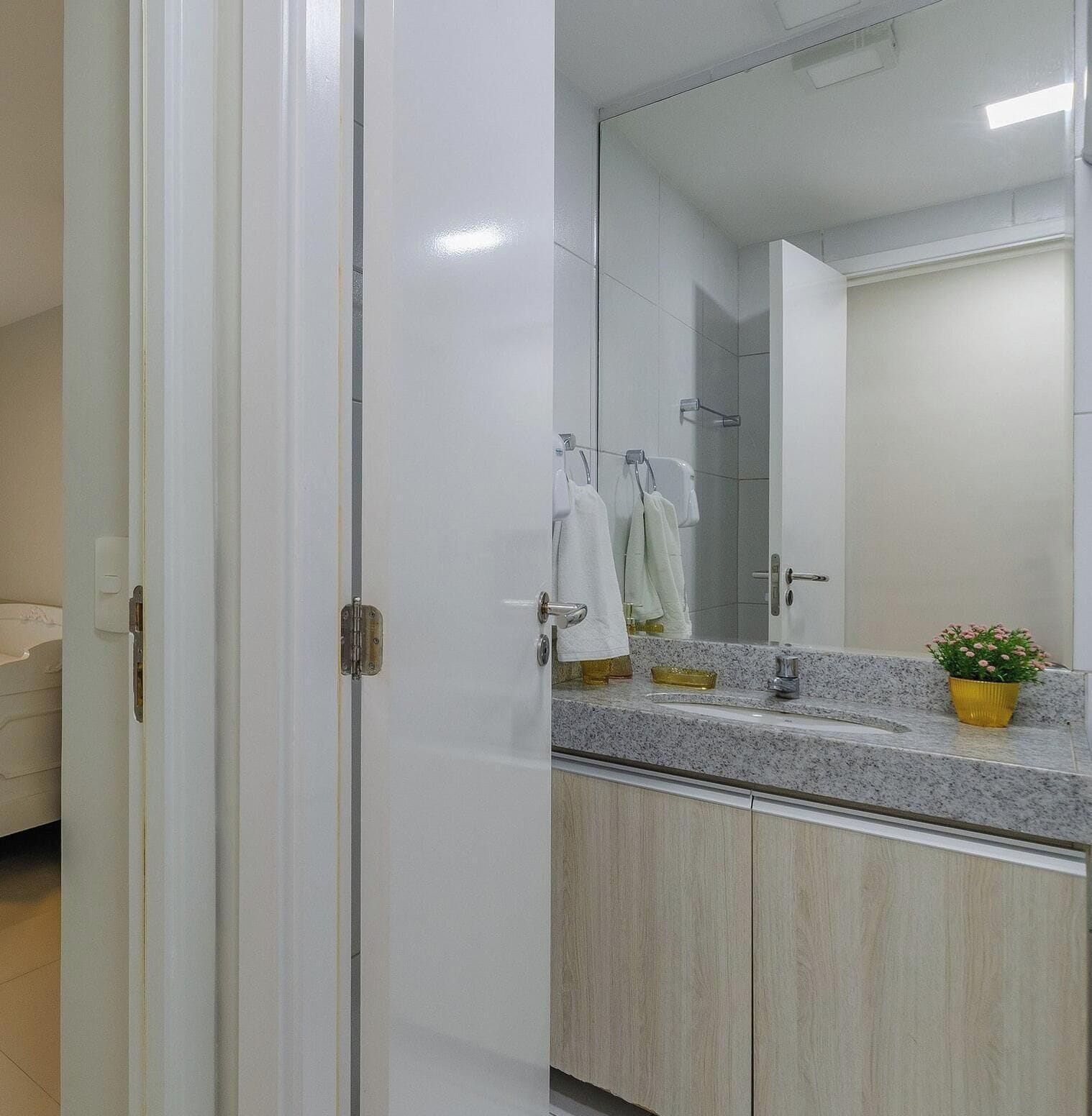 Un baño con lavamanos doble, espejo, planta en maceta y toallero.