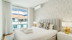 Une chambre d’hôtel avec un grand lit, deux tables de chevet, une fenêtre avec des rideaux et une vue sur un immeuble doté d’une piscine.