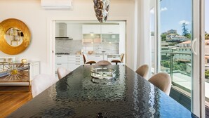 Une cuisine moderne dotée d’un grand îlot central, d’un coin repas avec une table noire et d’une vue sur les bâtiments à travers de grandes fenêtres.
