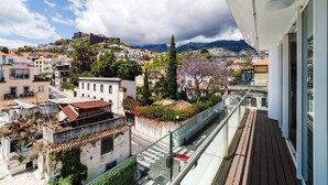 Un balcon offrant une vue sur un paysage urbain historique, avec notamment un édifice ressemblant à un château perché sur une colline et un ensemble de bâtiments résidentiels.