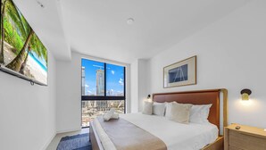 A hotel room with a large window, a bed, a nightstand, and a framed picture on the wall. - Luxe 1-BR at Miami Worldcenter | Skyline (Miami)
