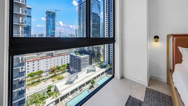 A hotel room with a large window offering a city view, a bed, and a small pool area. - Luxe 1-BR at Miami Worldcenter | Skyline (Miami)