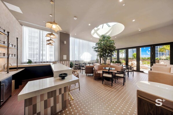 A modern kitchen with a central island, dining area with sofas, and a large window with a view of buildings. - Elite 1BR in Miami Worldcenter (Miami)