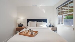 Ein Hotelzimmer mit einem großen Bett, einem Nachttisch mit Lampe, einem Tablett mit Frühstücksgebäck und einem Fenster mit Blick auf Grünflächen.