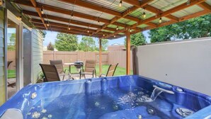 Ein Whirlpool unter einer überdachten Terrasse mit Holzbalkendecke und Stühlen.
