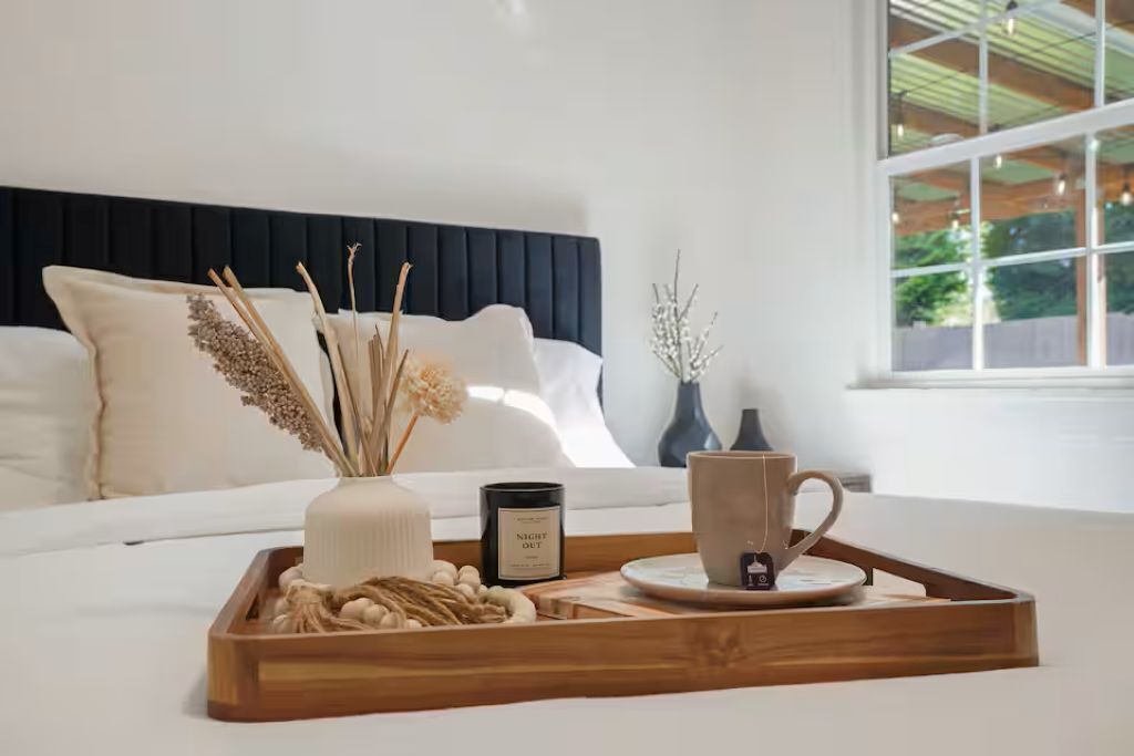 Une chambre à coucher avec un lit, une table de chevet sur laquelle est posée une bougie, un plateau avec une tasse et une fenêtre donnant sur un beau paysage.