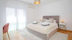 Quarto moderno com uma cama grande, uma mesinha de cabeceira, uma cadeira e um lustre.