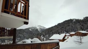 A wooden cabin with a balcony, surrounded by snow-covered trees and a mountain in the background. - Studio Apartment 'Le Refuge Douillet' with Mountain View and Private Terrace (La Plagne Tarentaise)